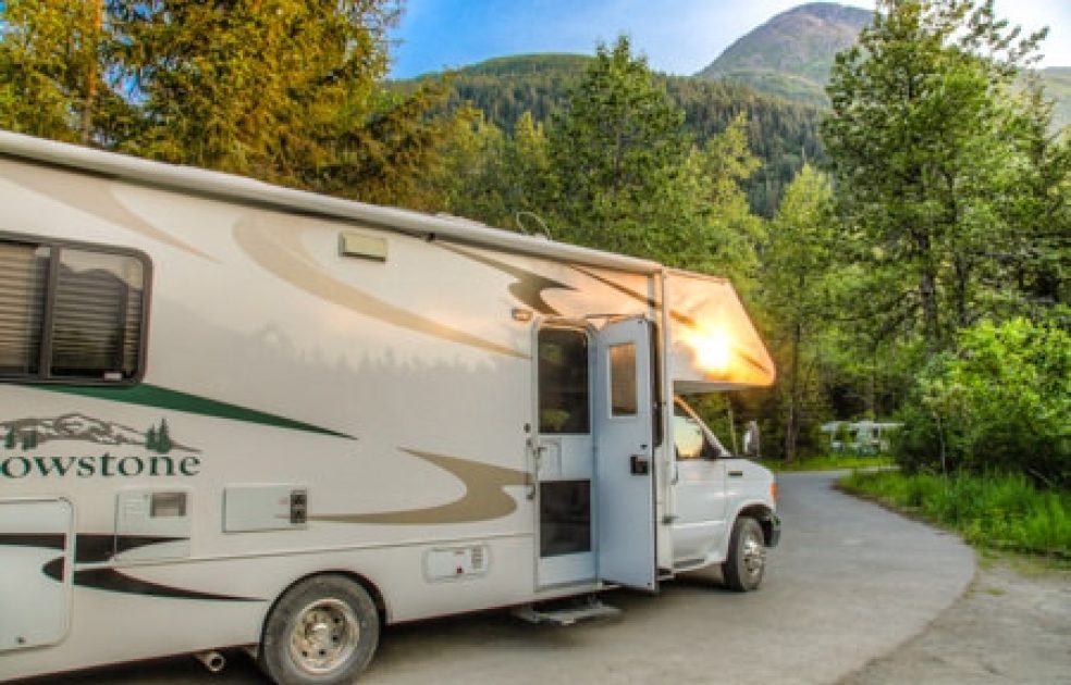 A Class C motorhome driving down a scenic highway in Alaska with mountains in the background