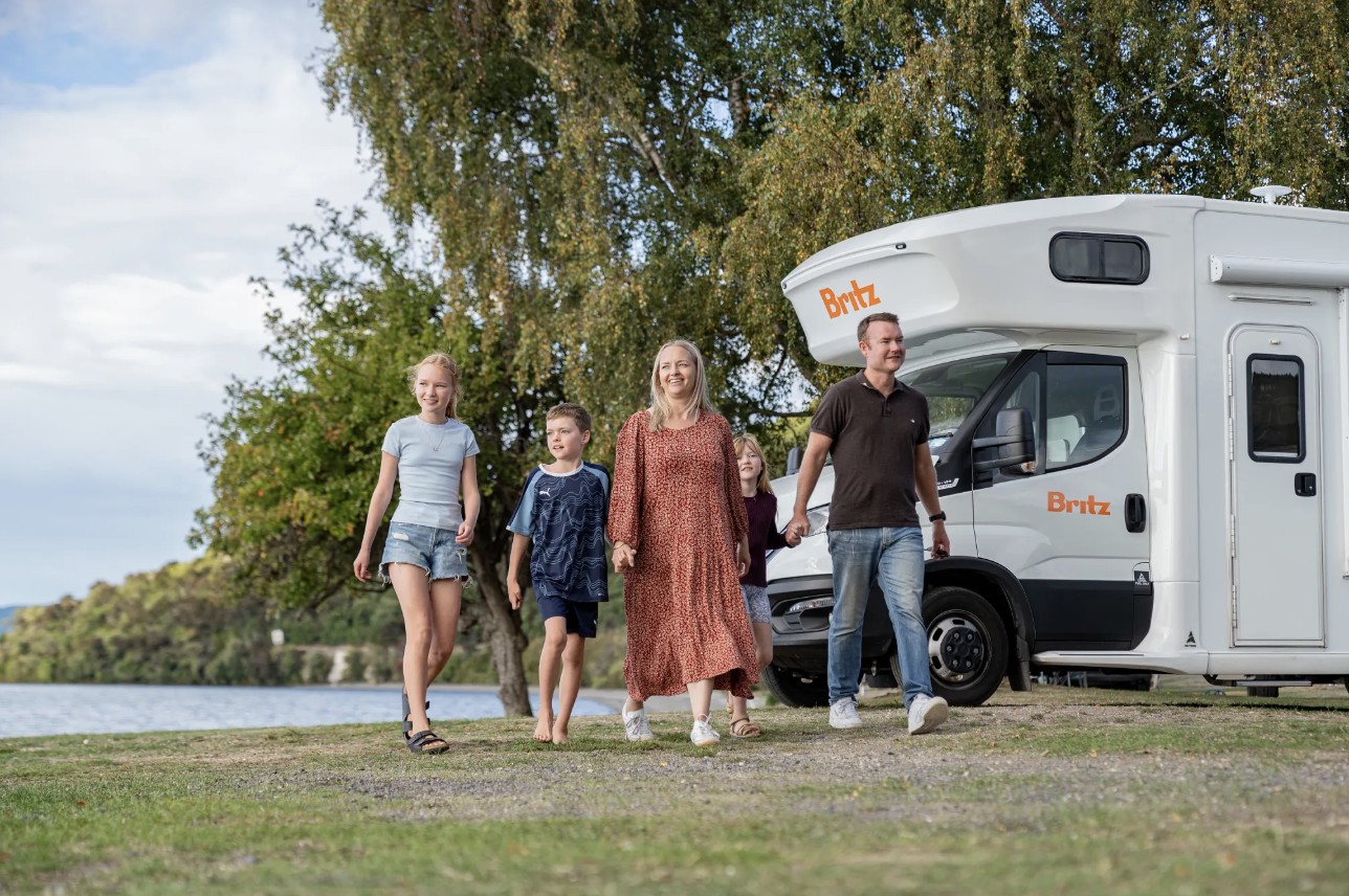 Family enjoying the outdoors with a rented Britz Class C Motorhome parked by a beautiful lake