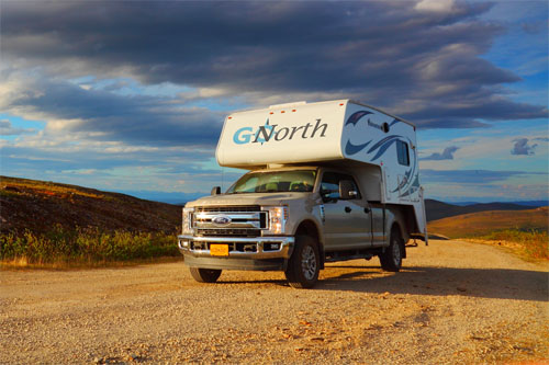 A Ford Truck Camper with 'G North' branding parked on a scenic dirt road