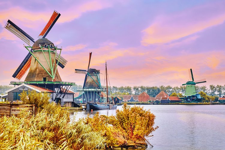 A bustling Amsterdam canal scene with boats and historic gabled houses reflecting in the water