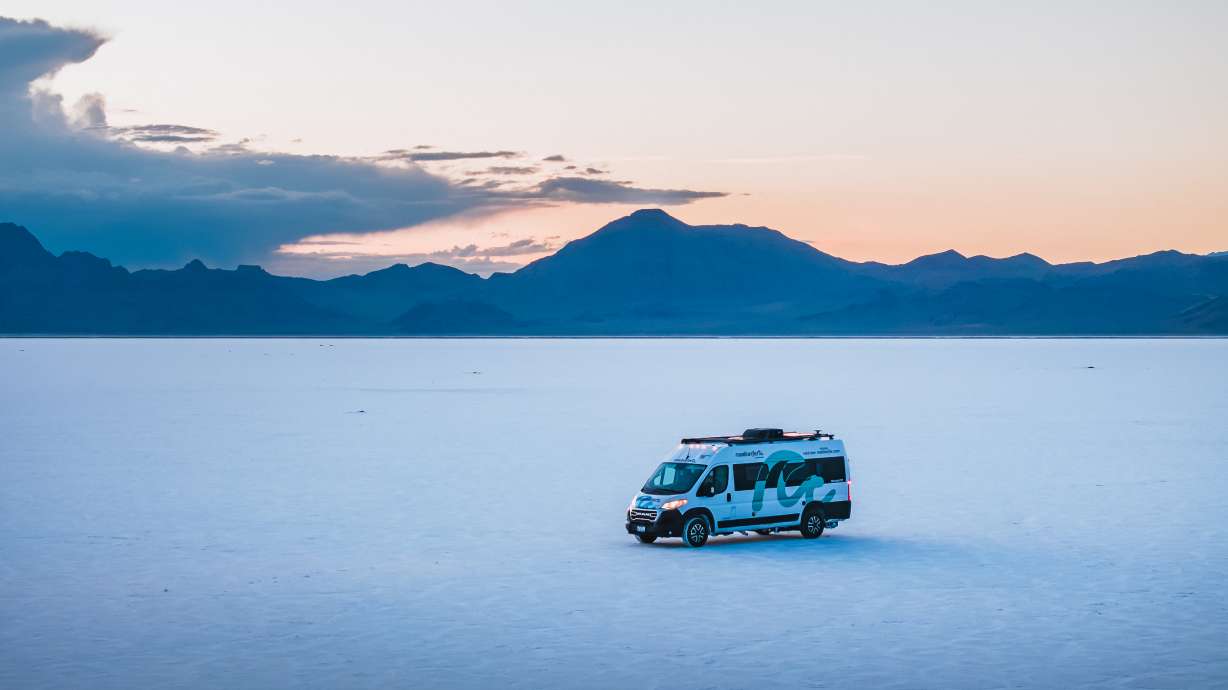A Class C motorhome driving on a scenic highway with mountains in the background